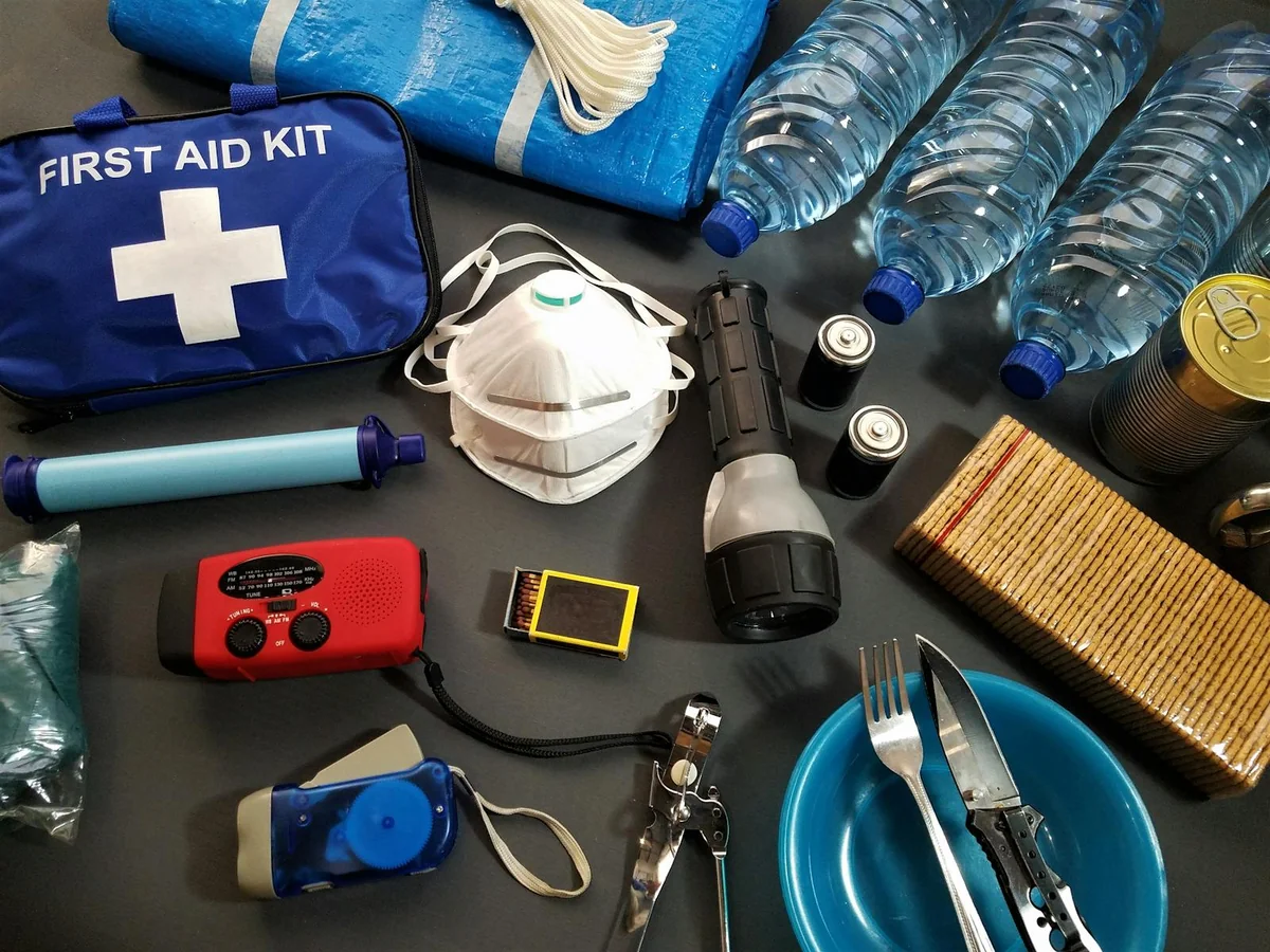 Kit di emergenza 72 ore disposto su un tavolo di legno con acqua, cibo, torcia e primo soccorso